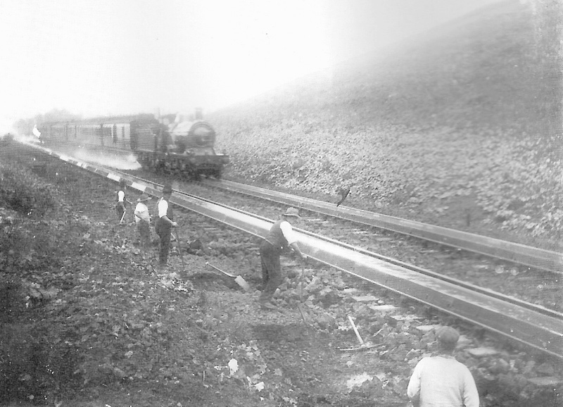 A GWR 4-2-2 Dean Single on a Birmingham express service is seen picking up water as it passes a P&W gang working on the drainage to the troughs