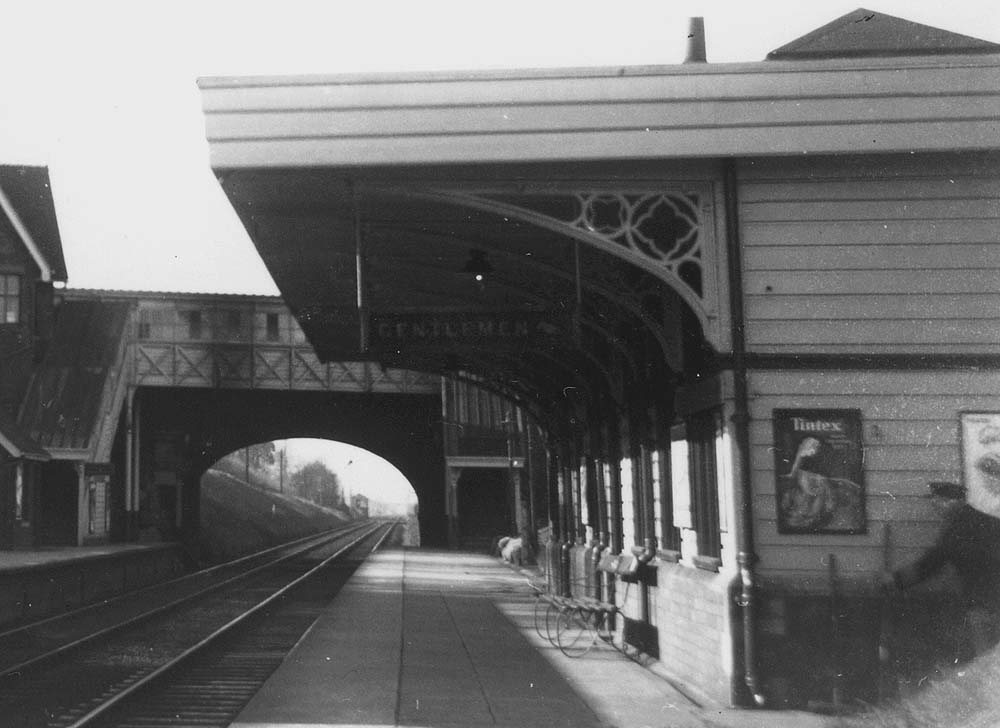 Close up showing the up platform building, the passenger footbridge, gas lights suspended from the canopy and the very basic bench seating