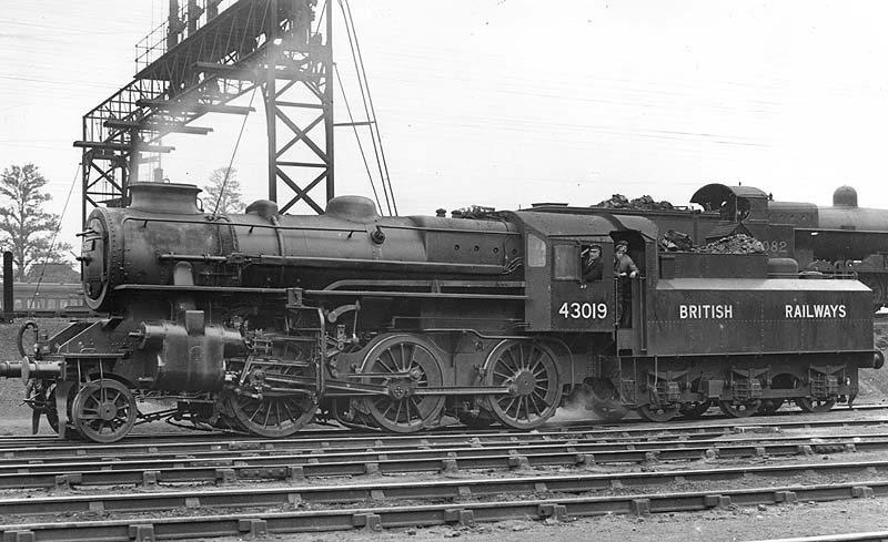 Ex-LMS 4MT 2-6-0 No 43019 is seen on shed standing alongside the Rugby to Stafford mainline whilst in the background an ex-LNWR 7F 0-8-0 'Super D' runs light engine to Rugby