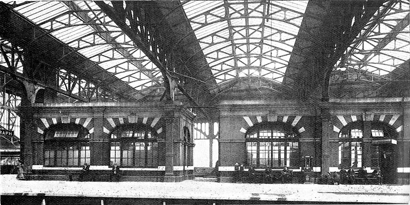 The striking buff and red terracotta elliptical arches on the platform buildings below the glazed transverse roof bays