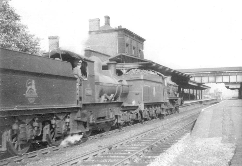 A pair of unidentified engines, a 4-6-0 Castle and an outside framed 4-4-0 pass through the station