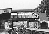 Close up showing the covered station footbridge and road bridge behind