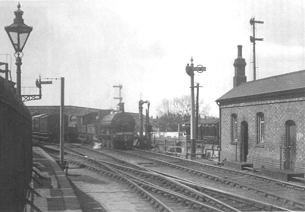 A GWR' 1076' class 0-6-0ST is seen at the head of a short goods train standing adjacent to the water column