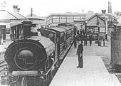 A GWR 0-6-0ST locomotive stands at the station's up platform with express headlamps on the buffer