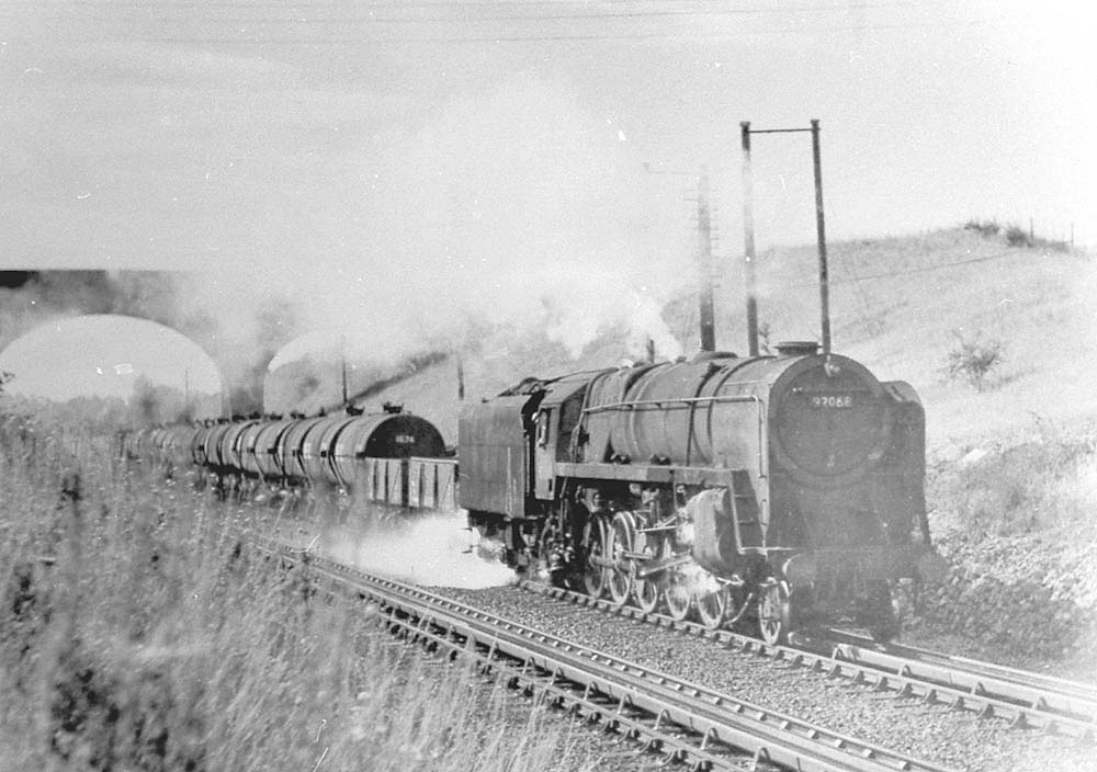 British Railways Standard Class 9F 2-10-0 No 92068 picks up water at the head of a Class F express freight service