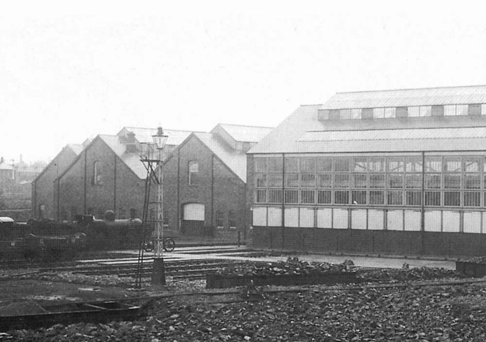 Close up showing a GWR 0-6-0 'Dean goods' locomotive standing on one of the approach roads in front of the sheds with the doors to the repair shops on the right