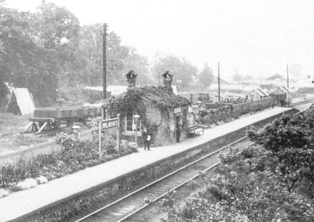 Close up showing the simple station structure on the platform and the open and covered wagons in the goods yard behind