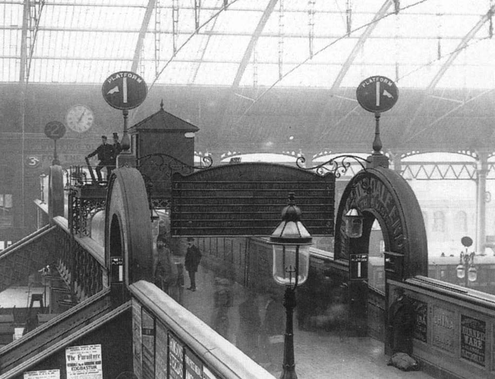 Close up of the passenger footbridge showing the departure indicator board suspended over head and in between the steps to Platform One