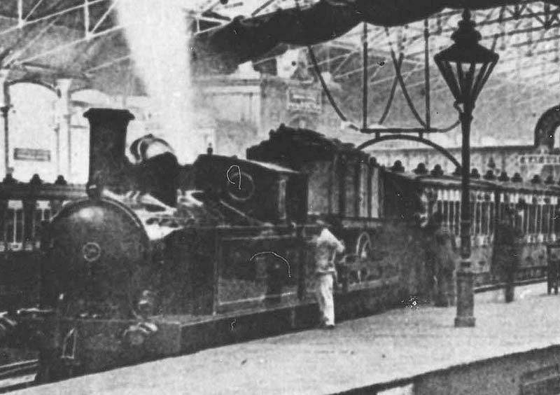 Close up of the unidentified LNWR 2-4-2T locomotive at the head of a local passenger service with a flat truck behind the bunker loaded with a road cart