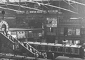 Close up of the passenger footbridge as passes through Platform 3's station structure showing the large station sign and the clock above the walkway