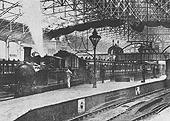 Close up of the unidentified LNWR 2-4-2T locomotive at the head of a local passenger service with a flat truck behind the bunker loaded with a road cart