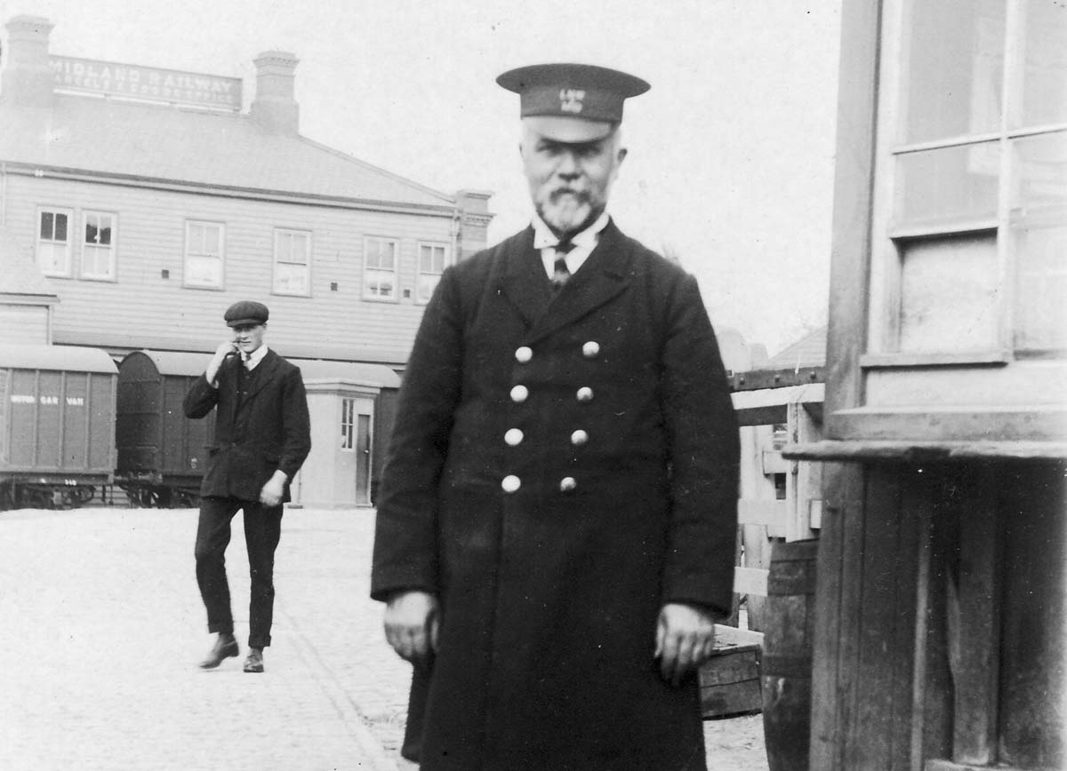 A photograph of Mr John James King, Chief Cartage Foreman, standing beside the LNWR cartage office with the MR shed and offices in the background