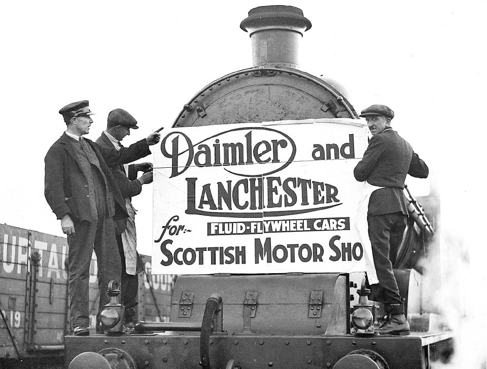 Workmen from Daimler and Lanchester Cars and the LMS attach a poster to the smokebox of the ex-LNWR 4-6-0 locomotive