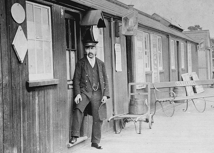 Close up of Flecknoe station's single-storey building and its miscellaneous furniture and fixings including station clock, porter's barrow and oil lamps