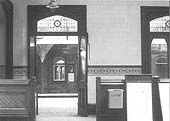 An internal view of the booking hall looking towards the platforms showing the station's tiled walls and stained glass windows