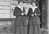 Photograph of two L&NWR lady ticket collectors standing in front of a poster advertising Nuneaton station's restaurant