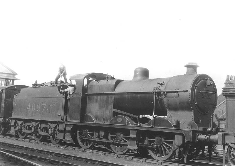LMS 0-6-0 4F No 4087 is seen with its crew breaking up coal in the tender whilst being piloted at the head of a stopping passenger train