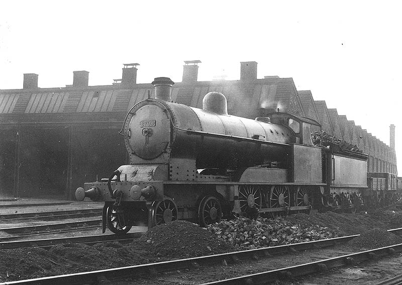 Ex-LNWR 4-6-0 No 8799, a 19 inch goods engine, is seen at the head of a train of empty mineral wagons passing alongside the shed