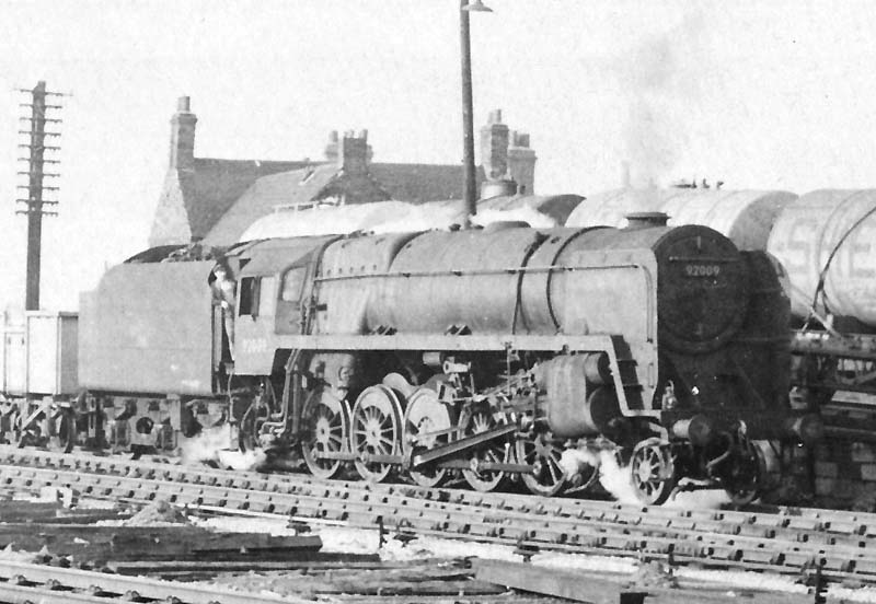 British Railways Standard class 9F No 92009 is seen heading a mineral train out of the marshalling yard as an oil train is being shunted over the  yard's hump