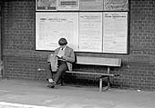 A young passenger is engrossed in his paper as he waits on platform one for his train home on 13th August 1964