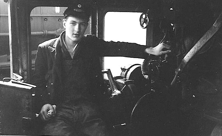 David Bailey (1946 - 1981) poses for the camera as he sits on the driver's side inside an unidentified locomotive