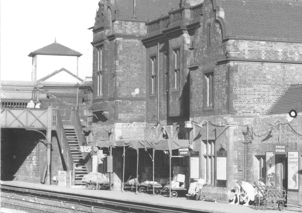 Close up showing the platform side of Livock's main station building and an assortment of  trollies with both parcels and mail bags