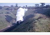 An BR 2-10-0 9F locomotive emerges from the tunnel at the head of a freight train on 16th October 1965