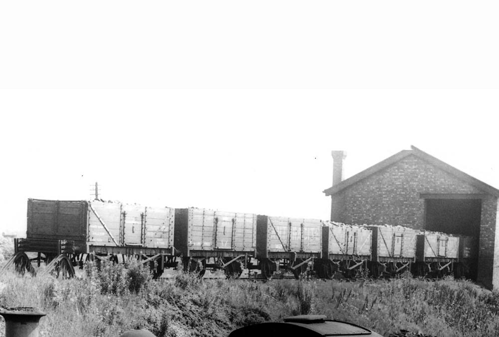 A line of locomotive coal wagons standing on the embankment at the end of the coaling shed's siding