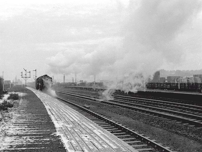 An unknown British Railways Standard Class 9F 2-10-0 locomotive runs tender first and light engine through the station's up platform