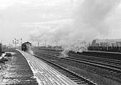 An unknown British Railways Standard Class 9F 2-10-0 locomotive runs tender first and light engine through the station's up platform