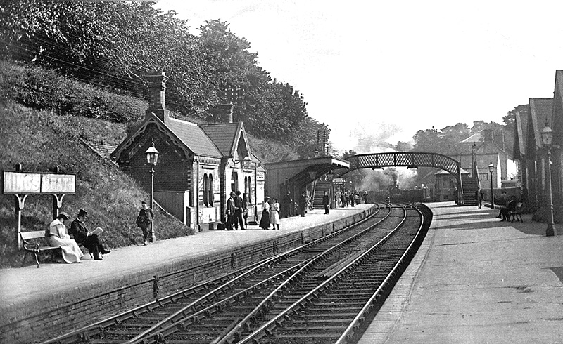 Looking towards Moseley with passengers waiting on the up platform as a down goods train approaches the signal box