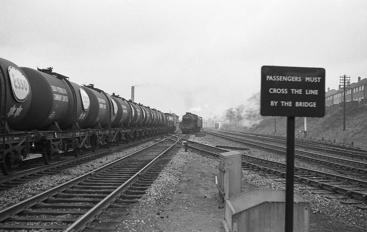 A down train of Esso Class B 4-wheel tank wagons passes Kings Norton goods yard as ex-MR 0-4-0 No 41535 and an unidentified ex-LMS 4-6-0 Black 5 locomotive approach the camera