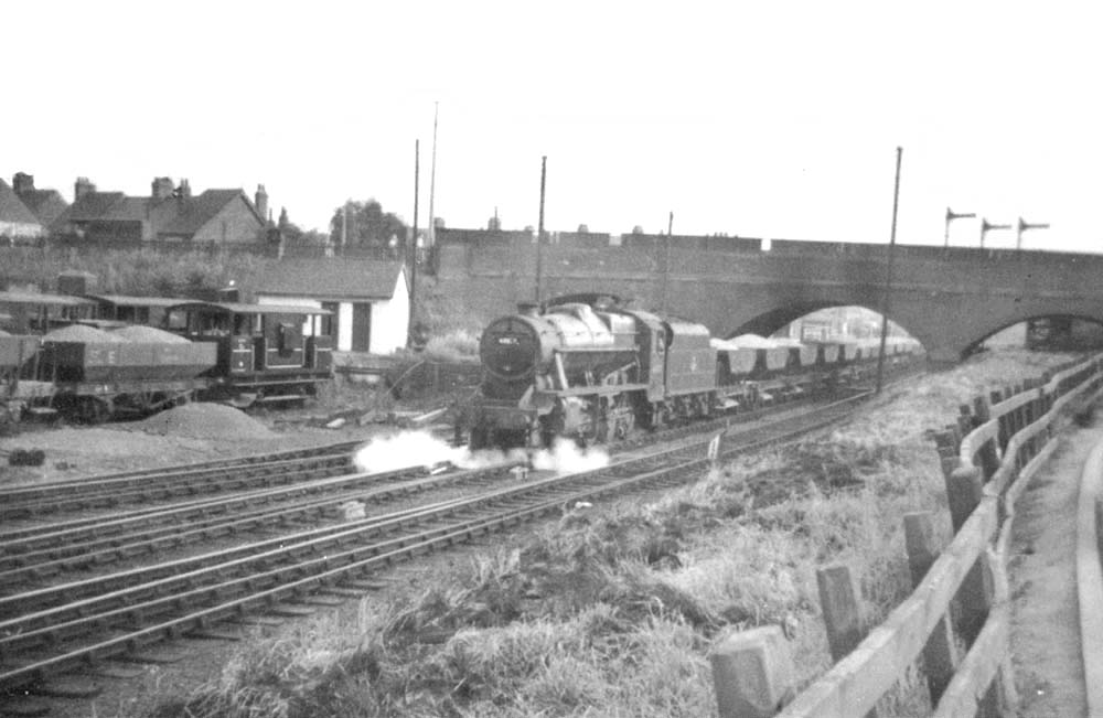 An unidentified ex-LMS 8F 2-8-0 locomotive sets backs 'wrong road' under the bridge with an engineer's ballast train