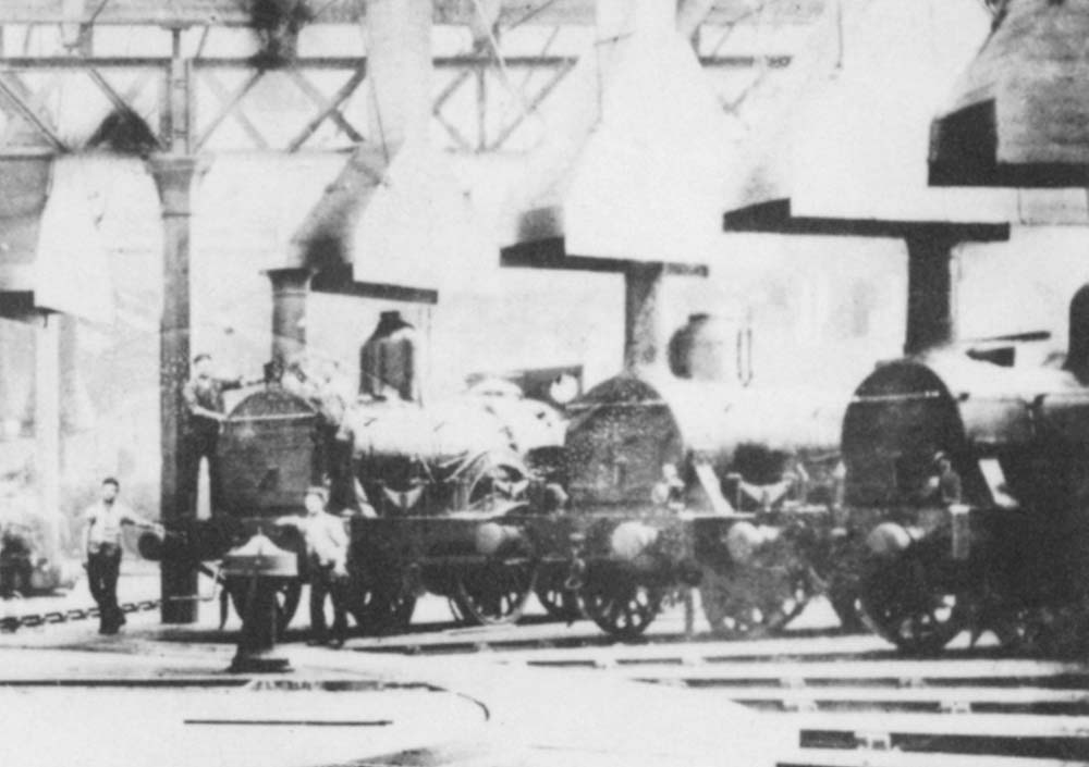 Close up showing the right-hand side of the shed with a number of Sharp Stewart 2-2-2 locomotives standing around the turntable and another hand-operated capstan