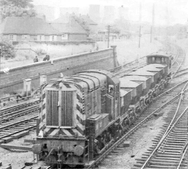 An unidentified British Railways Class 08 diesel electric shunting locomotive comes off the Kingsbury branch with a short ballast train