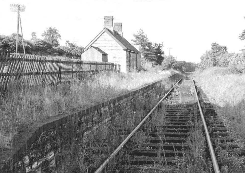 A reverse angle view along the still used but overgrown single line towards Stratford upon Avon with the disused station on the left