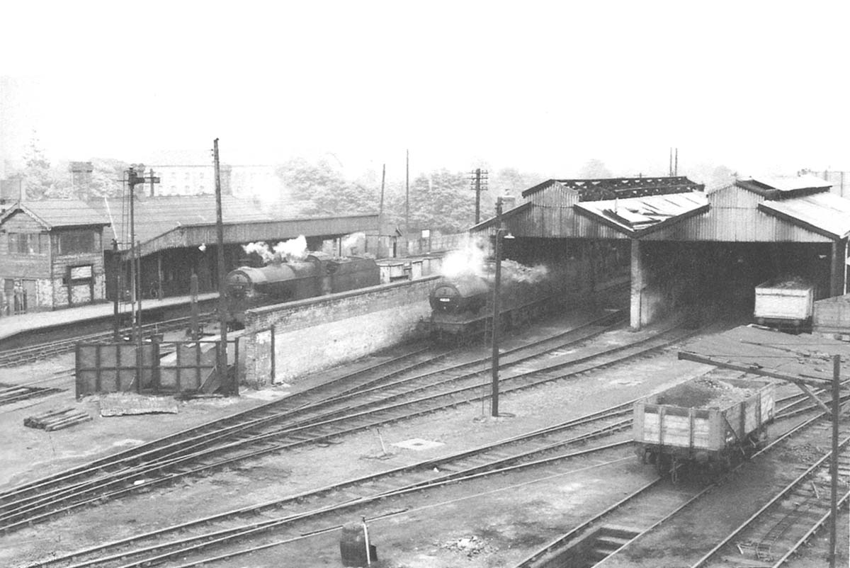 Ex-MR 3F 0-6-0 No 43223 stands in steam on shed as ex-MR 4F 0-6-0 No 43875 passes through Stratford upon Avon Station with a down freight on 2nd May 1957
