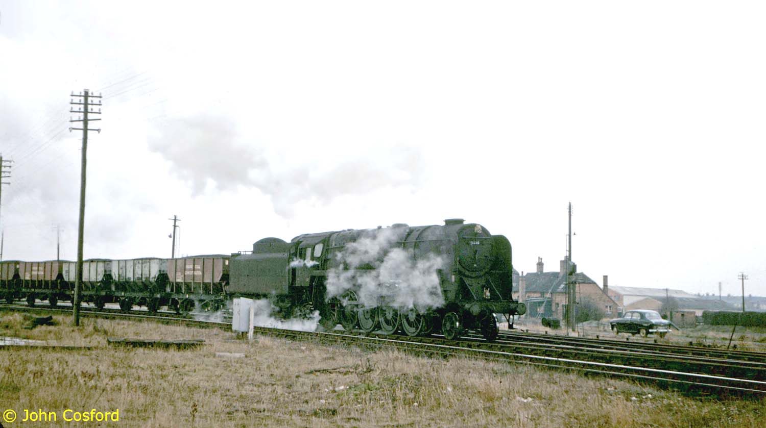 An unidentified British Railways Standard Class 9F 2-10-0 locomotive is seen with a Class H through freight of coal in the early 1960s