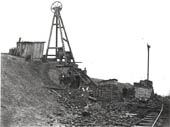Eight labourers pose for the camera alongside another timber framed headgear erected over a shaft