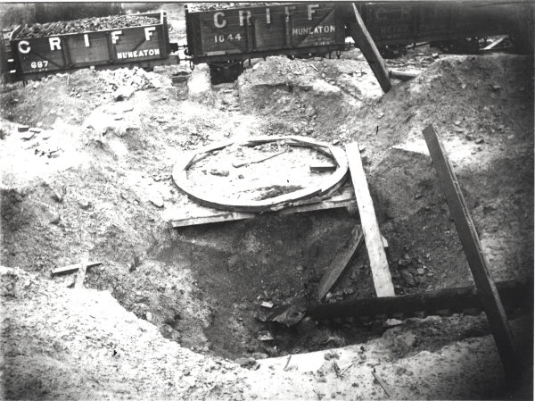 Looking down from the top of a spoil heap towards a section of circular timber shaft formwork