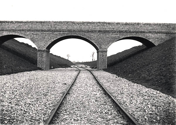 A line of contractor's temporary track snakes under a brick occupation overbridge near Staverton