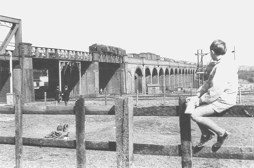 An unidentified British Railways Standard Class 9F 2-10-0 locomotive passes over the West Coast Main Line circa 1965